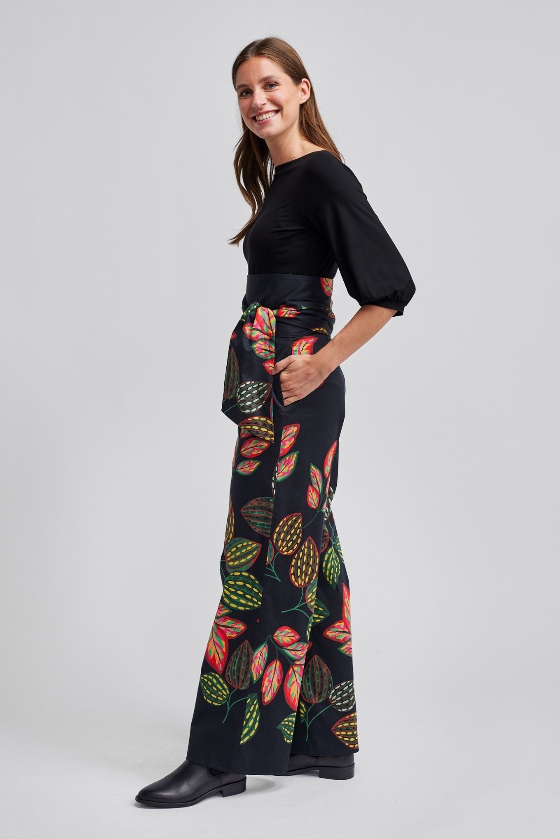 Model trägt schwarze Hose mit weitem Bein und Bindegürtel, Seitenansicht mit buntem Blätter-Print.