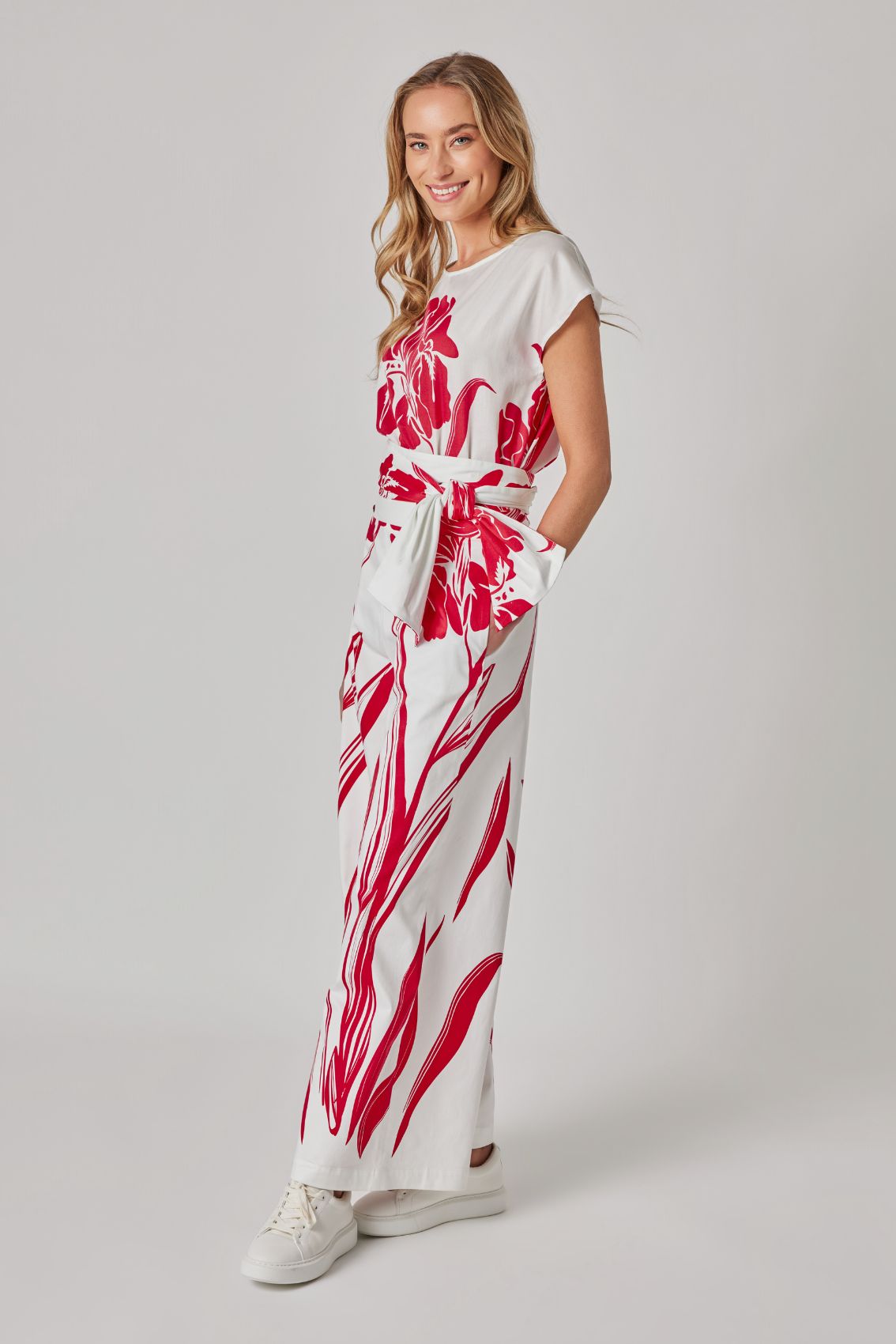 Model trägt weiße High-Waist Hose mit weitem Bein und Bindegürtel, Seitenansicht mit rotem Print.