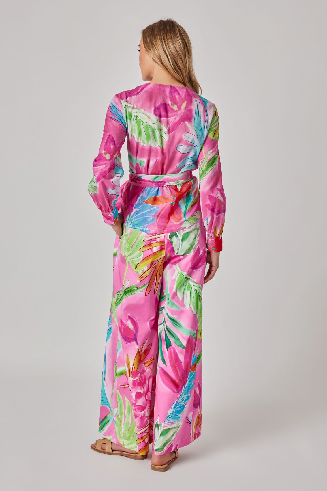 Model trägt pinke, weit geschnittene Hose mit floralem Print und hohem Wickelbund, Rückenansicht.