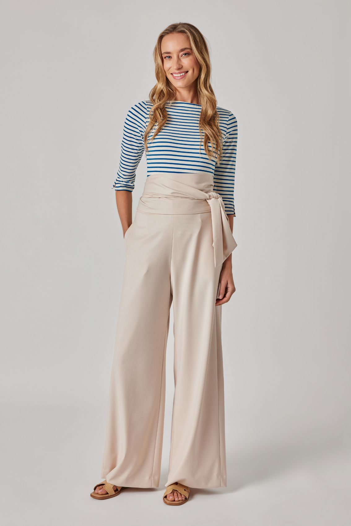 Model trägt blau-weiß gestreiftes 3/4-Arm Top und beige, weit geschnittene Hose mit Wickelbund, Frontansicht.