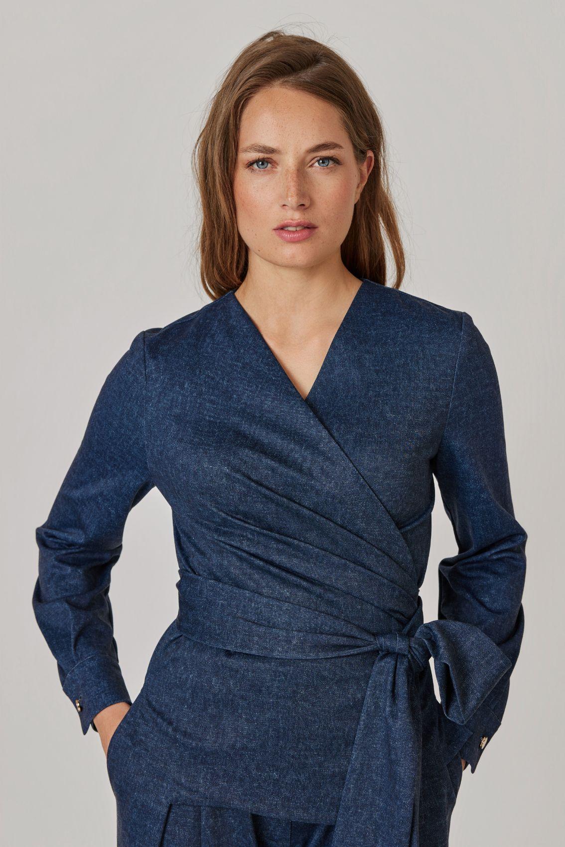 Model trägt Wickelbluse in Denim-Blau mit Bindegürtel zur passenden Hose, Frontansicht.