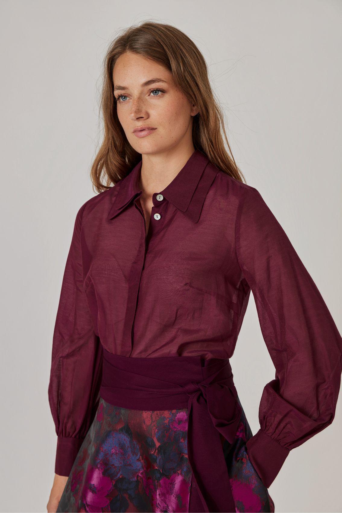 Model trägt Bluse in Aubergine mit Ballonärmeln und Manschette, Seitenansicht.