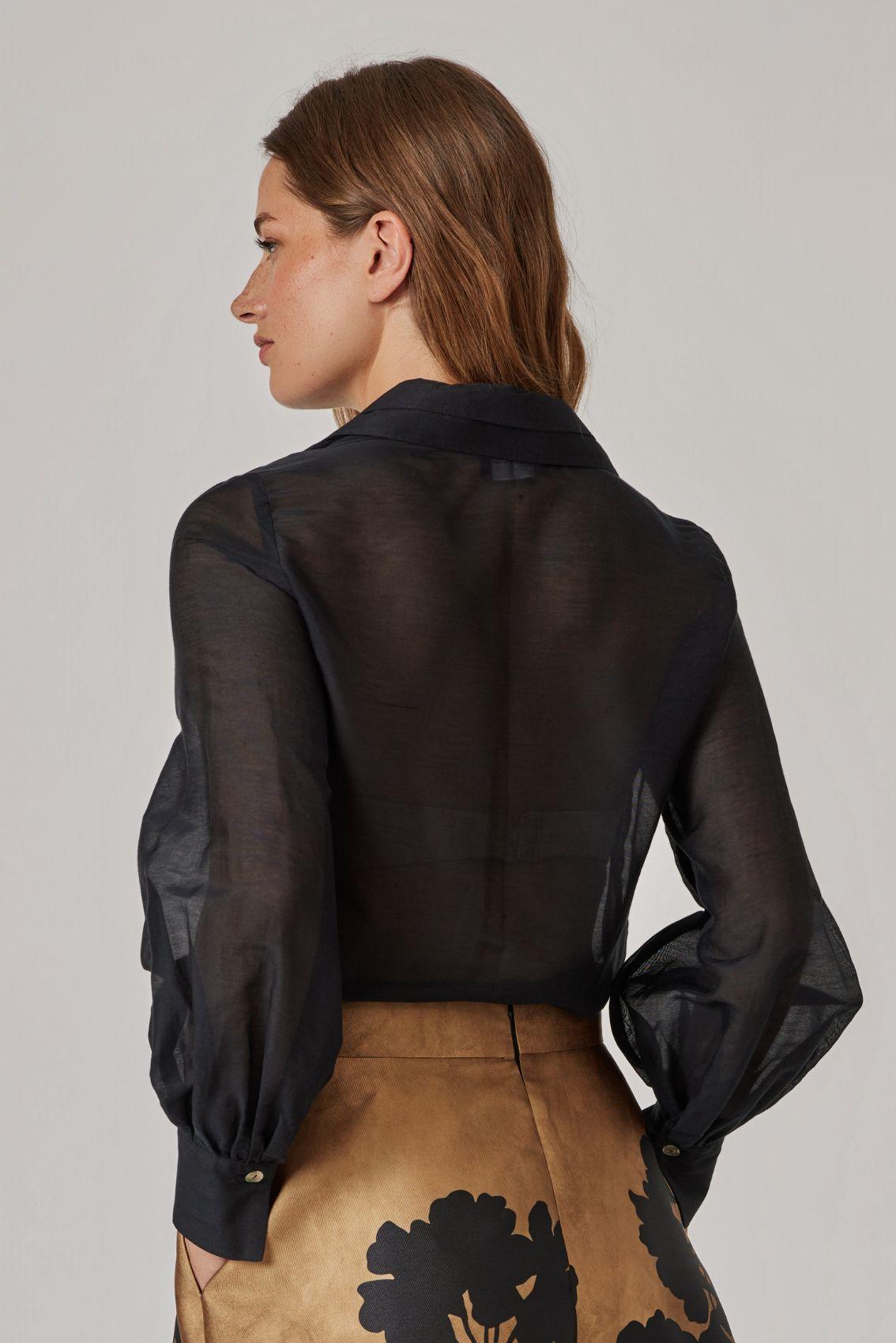 Model trägt schwarze Bluse mit leicht transparentem Stoff, Rückenansicht.