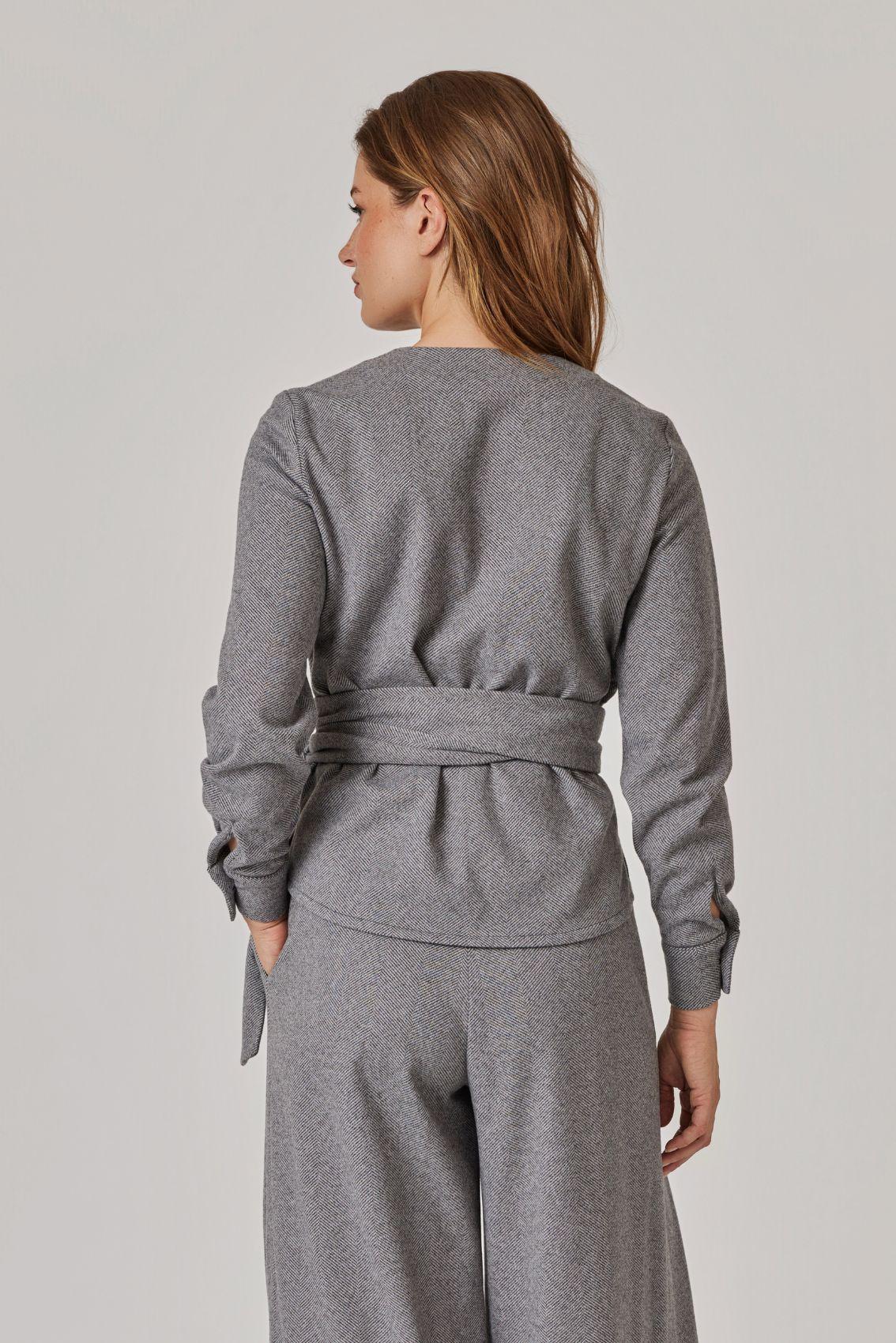 Model trägt Bluse in Grau meliert, Rückenansicht mit umlaufendem Bindegürtel an der Taille.