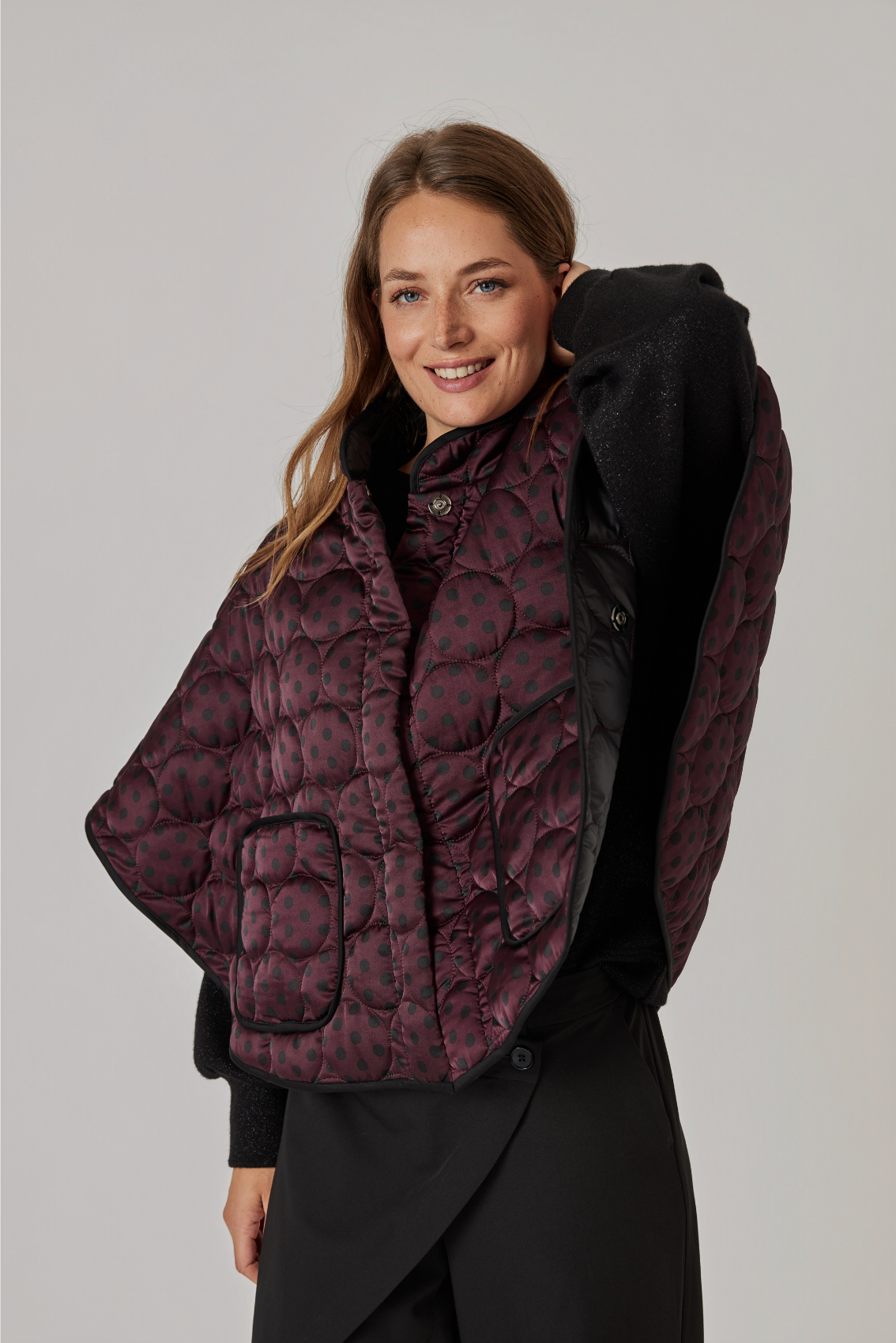 Model trägt das Cape in Bordeaux seitlich geöffnet, Seitenansicht mit Blick auf das schwarze Futter.