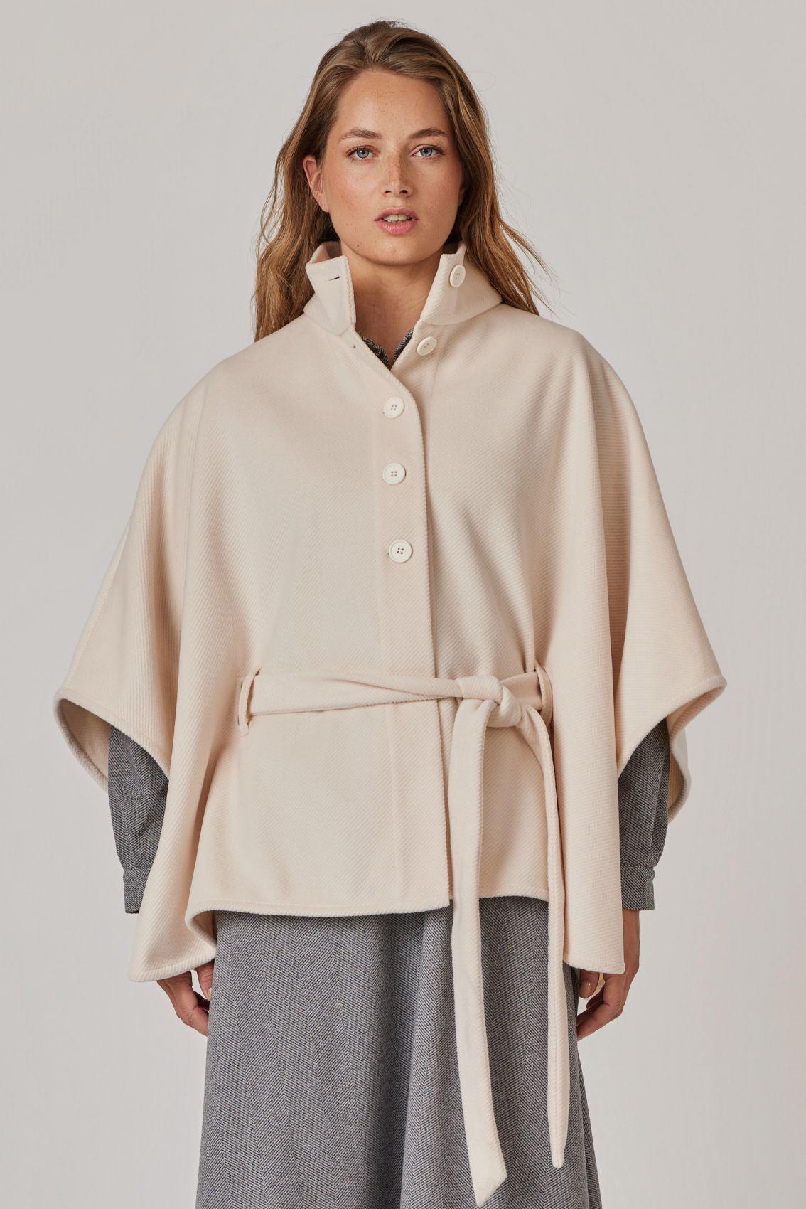 Model trägt Cape Creme mit Stehkragen und geschlossenem Bindegürtel, Frontansicht.