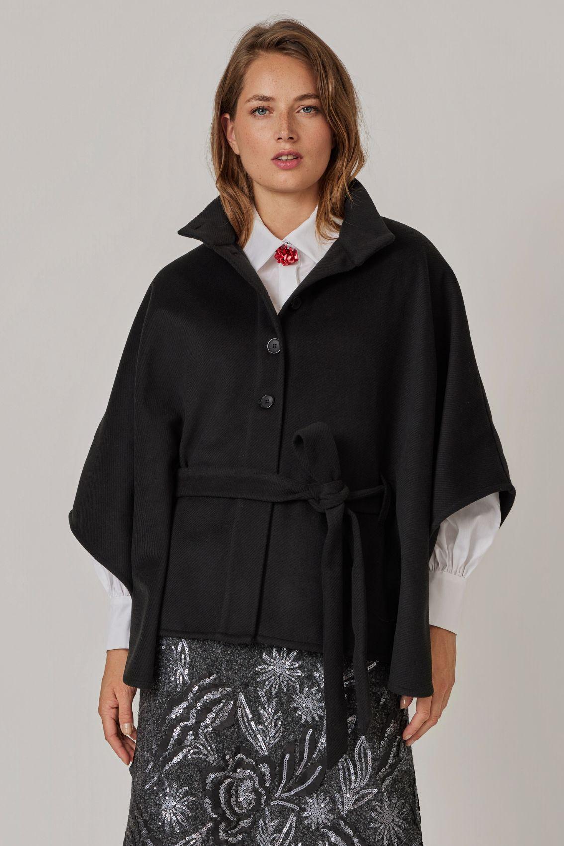 Model trägt Cape Schwarz mit Stehkragen und geschlossenem Bindegürtel, Frontansicht. 