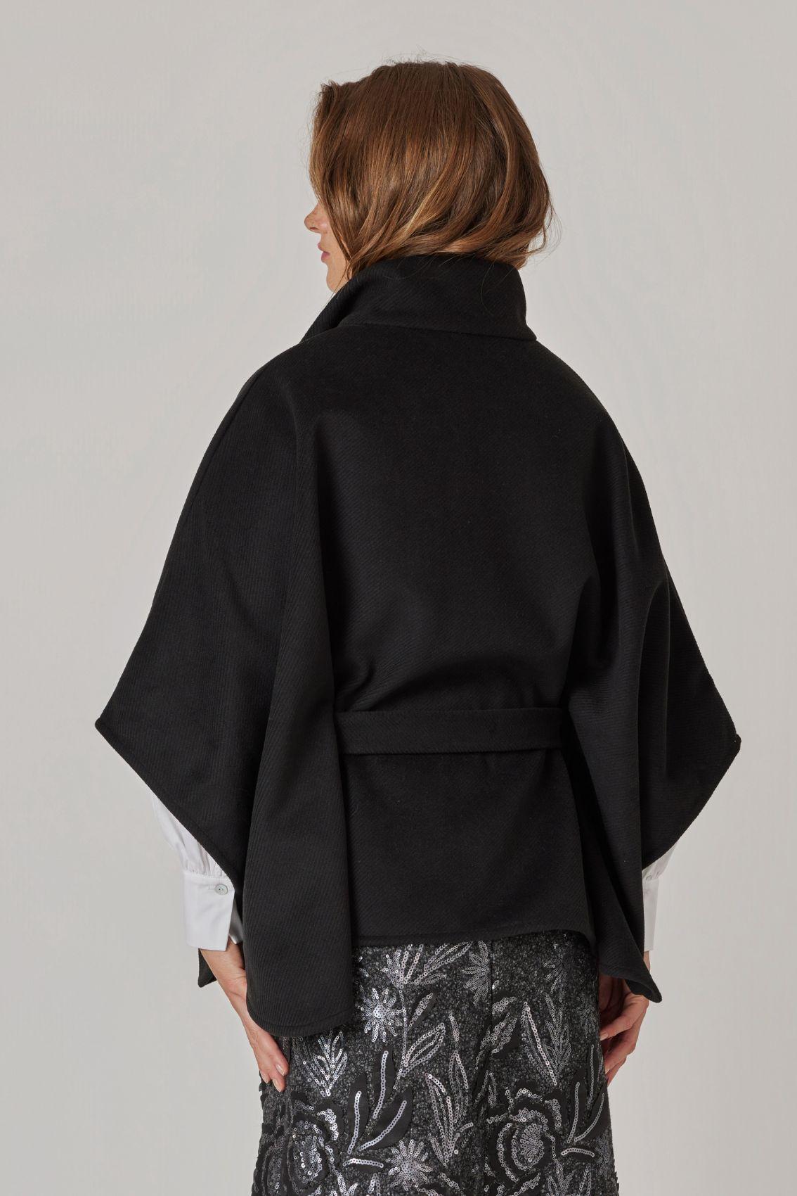 Model trägt Cape Schwarz, Rückansicht mit Bindegürtel und weitem Fall. 