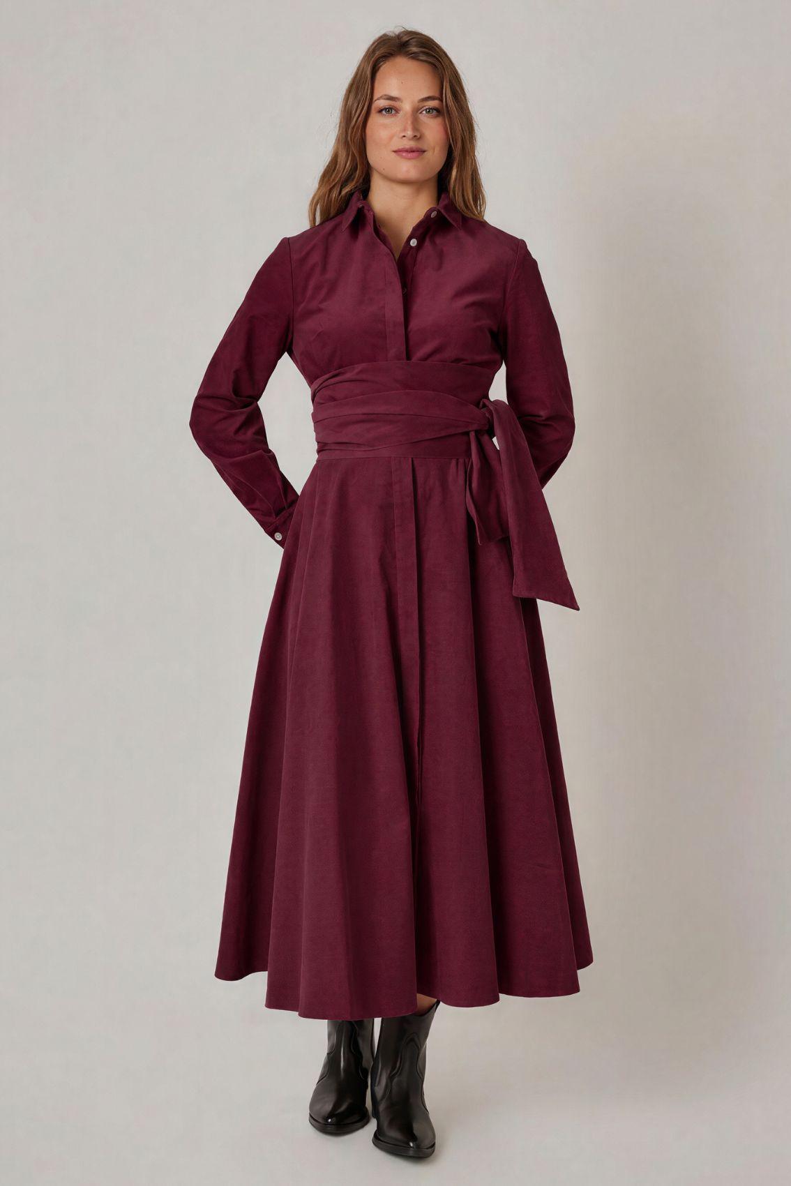 Model trägt auberginefarbenes Cordkleid mit Bindegürtel und Seitentaschen, Frontansicht.
