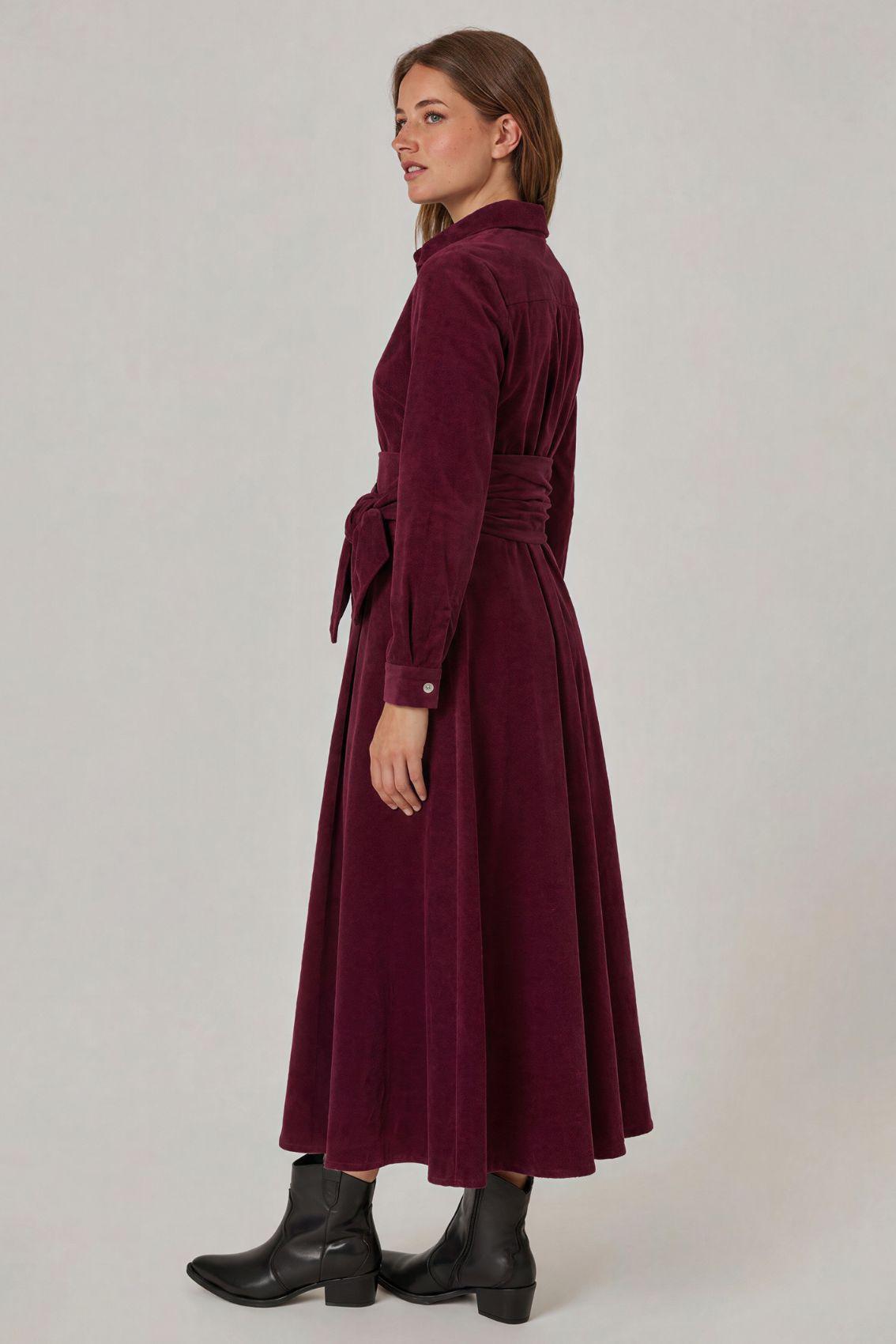 Model trägt auberginefarbenes Cordkleid, Rückenansicht mit geschwungenem Rockverlauf.