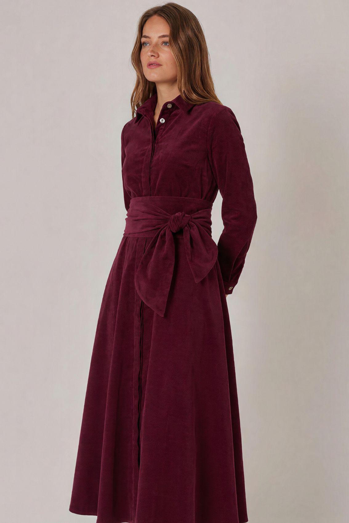 Model trägt Cordkleid in Aubergine, Seitenansicht mit taillierendem Bindegürtel.