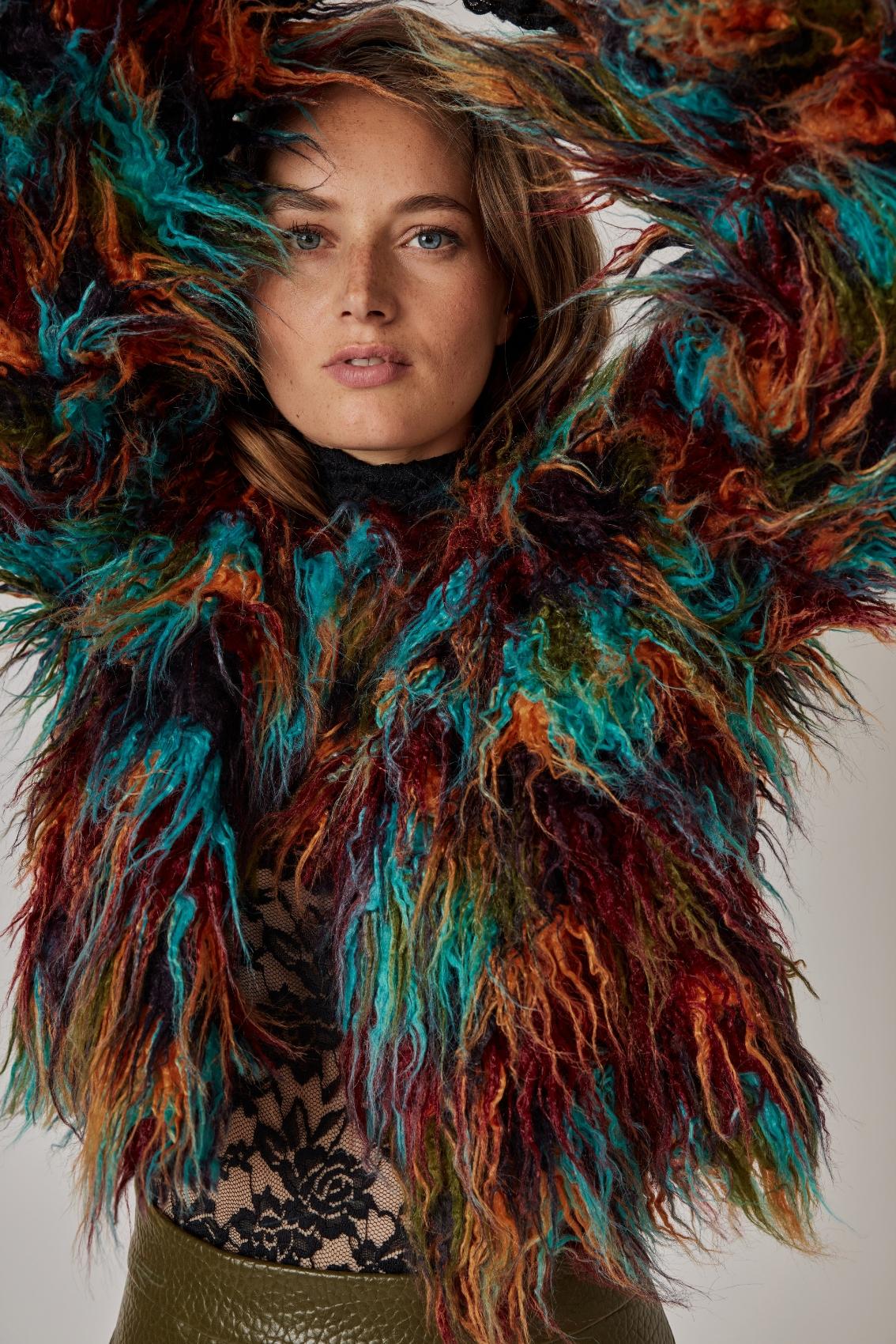 Model trägt mehrfarbige Kunstfelljacke mit erhobenen Armen, Close-up auf die langen Fasern in Türkis und Rost.