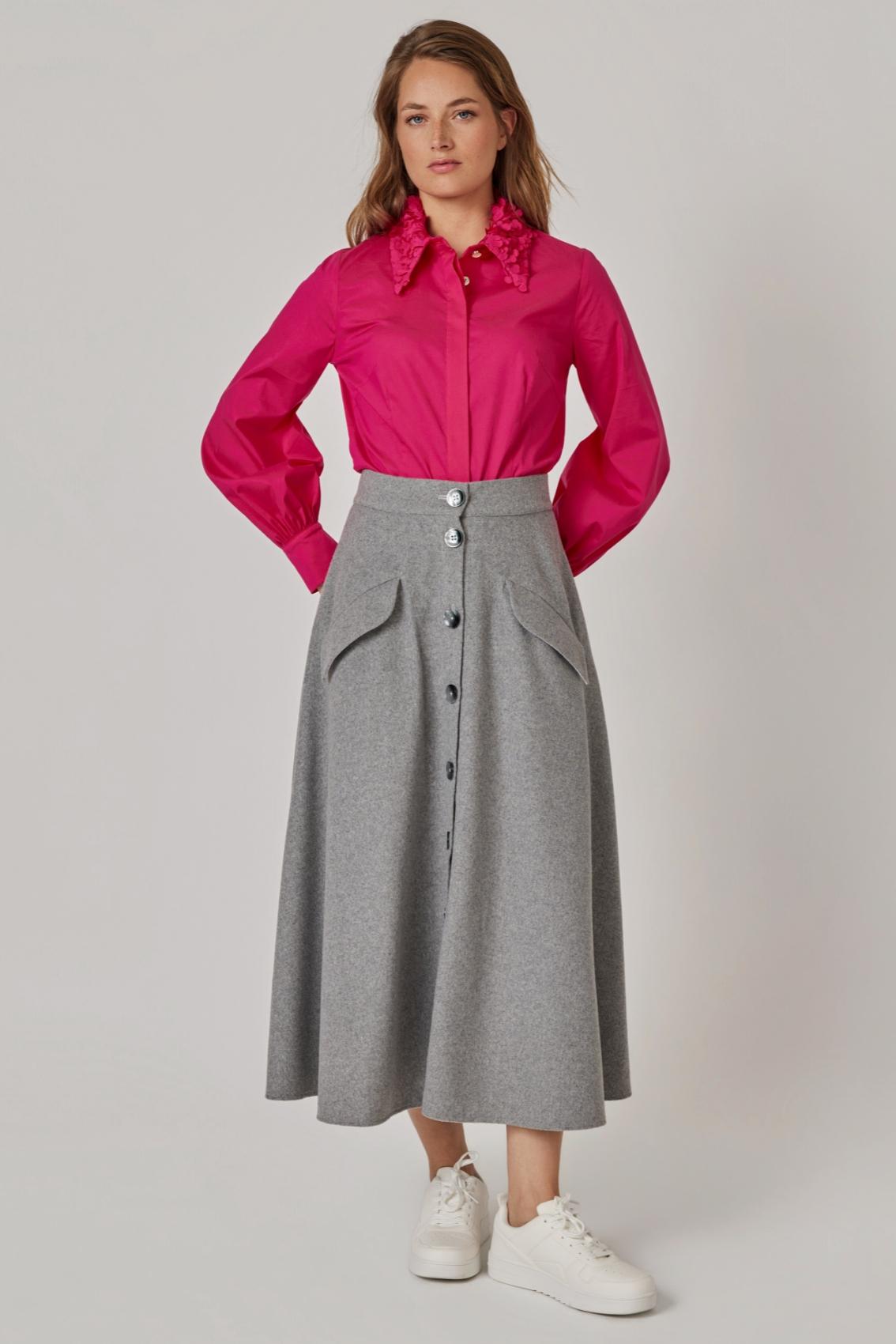 Model trägt grauen Maxirock mit Knopfleiste und Klappentaschen zu pinker Bluse und weißen Sneakern, Frontansicht.