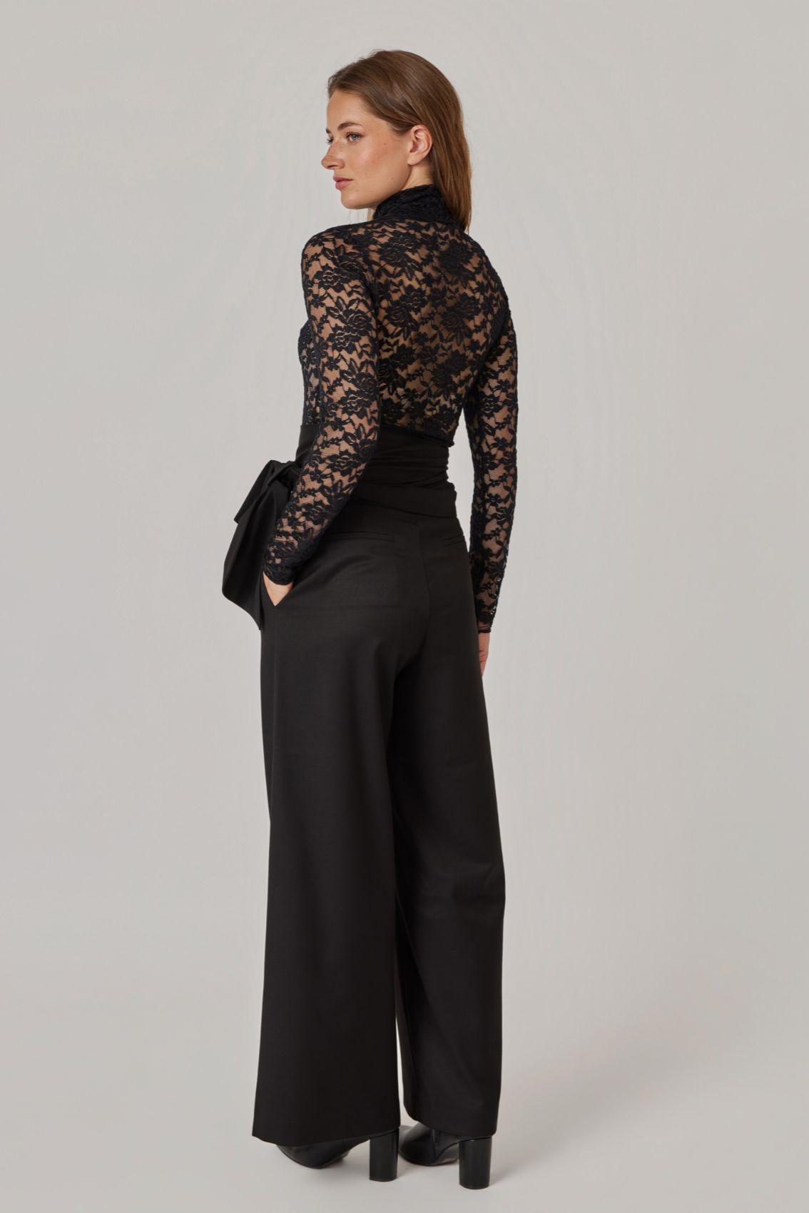 Model trägt die schwarze Hose in weitem Beinschnitt, Rückenansicht in voller Länge.