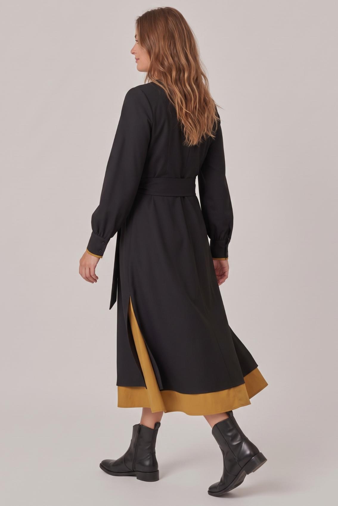 Model trägt schwarzes Kleid mit Bindegürtel und Ballonärmeln, Rückenansicht mit Unterrock in Safrangelb.