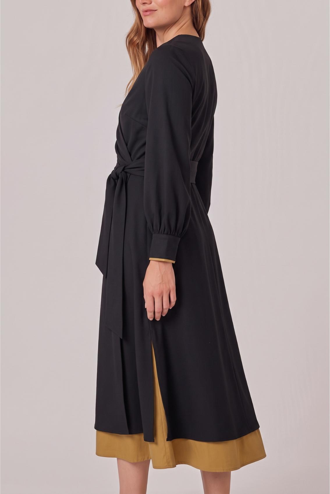 Model trägt schwarzes Kleid, Seitenansicht mit seitlichem Schlitz und sichtbarem Unterrock in Safrangelb.