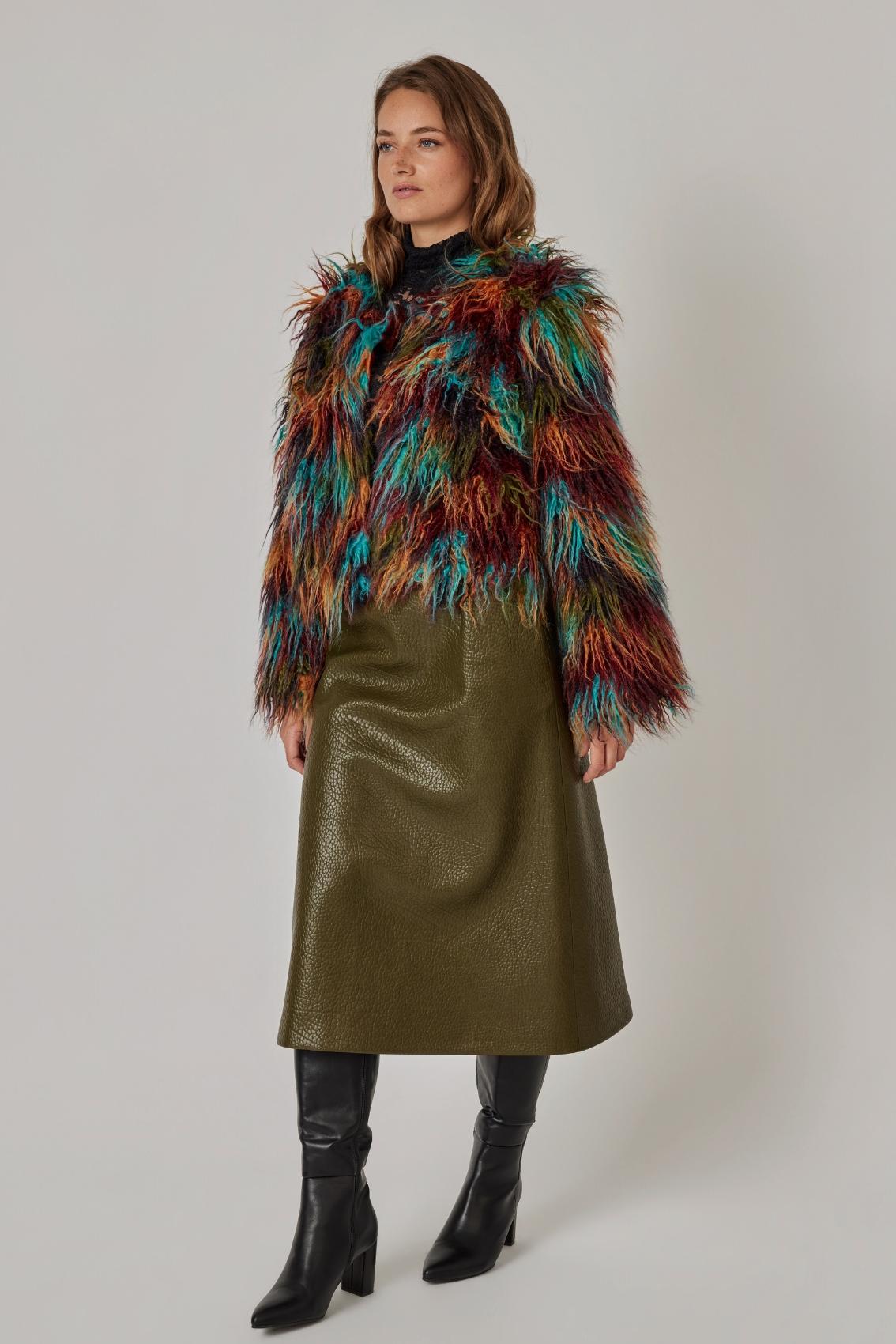 Model trägt mehrfarbige Langhaar-Jacke zu olivgrünem Midirock und schwarzen Stiefeln, Seitenansicht