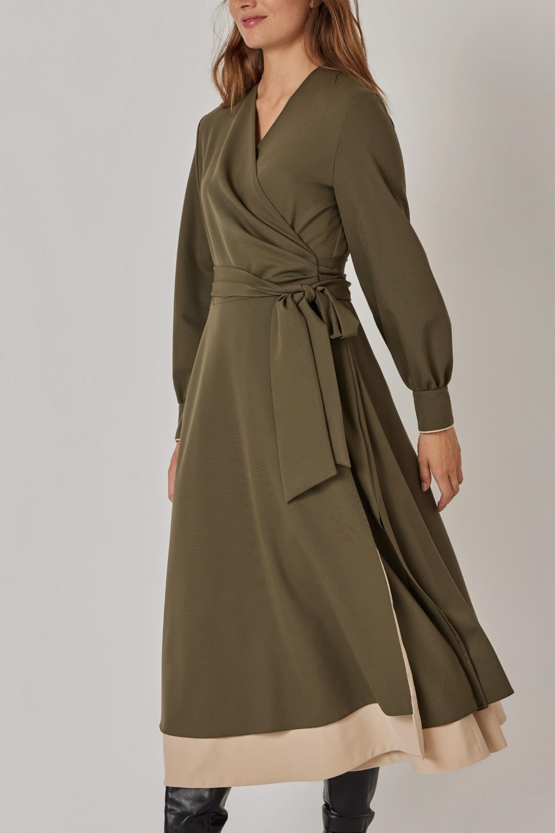 Model trägt olivfarbenes Midikleid mit Ballonärmeln, schräge Seitenansicht mit schwingendem Rock und Unterrock in Sand.