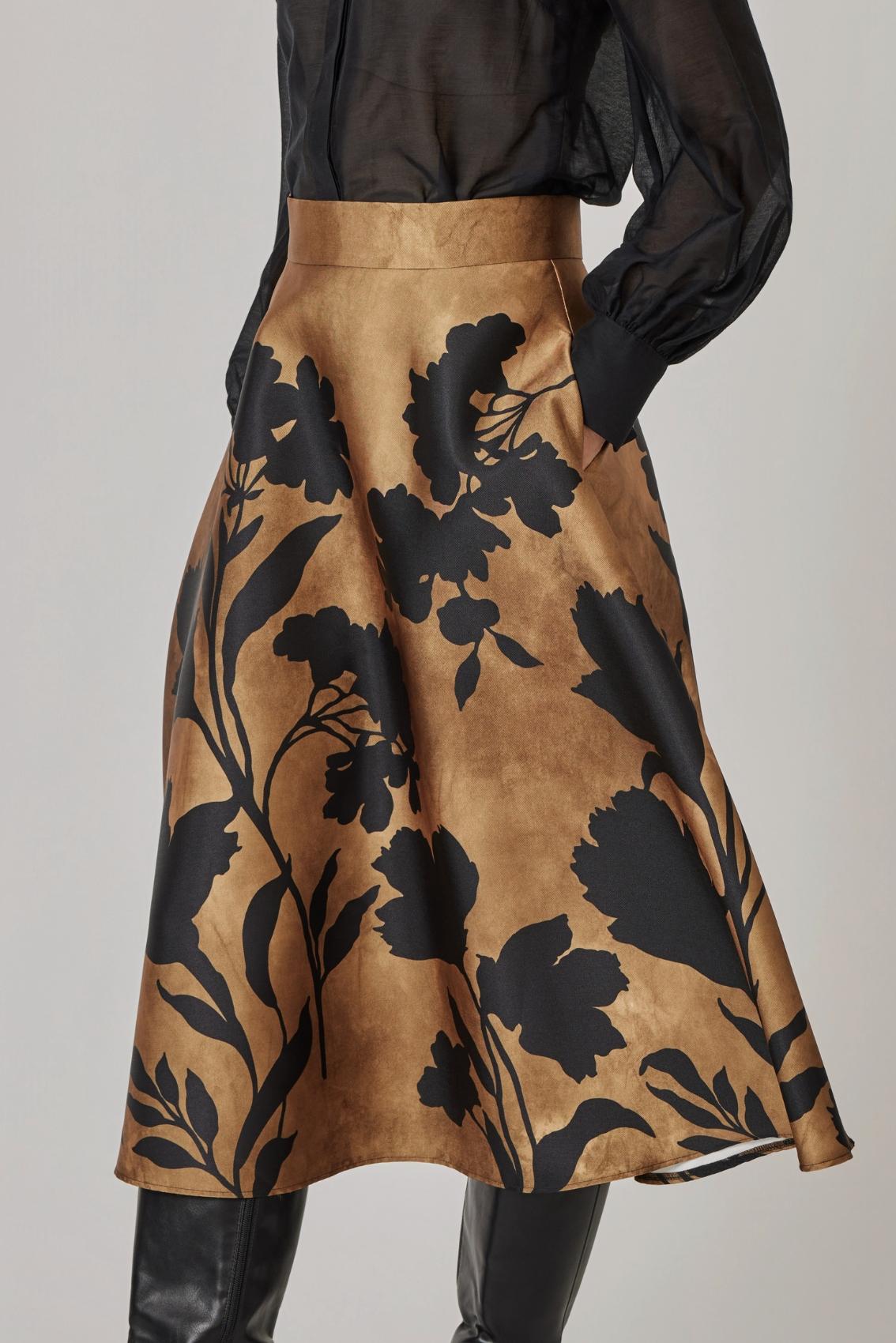 Nahaufnahme des Blüten-Scherenschnitt-Prints auf dem Midirock in Gold, mit Seitentasche.