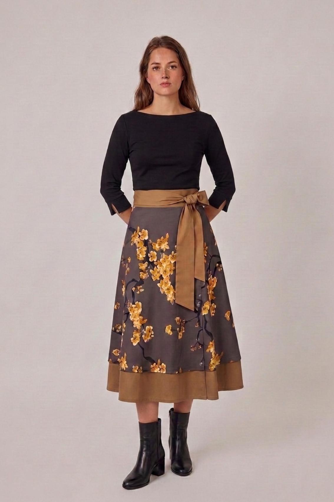 Model trägt Wickelrock mit goldgelbem Kirschblütenprint, schwarzes Oberteil und schwarze Stiefeletten, Frontansicht.