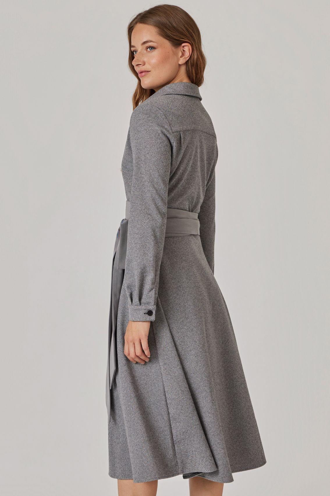 Model trägt Fischgrätkleid mit geknotetem Bindegürtel, Seitenansicht mit schwingendem Rockteil. 
