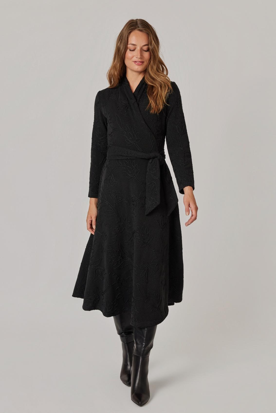 Model trägt schwarzes Strickkleid mit Blumenstickerei, Wickel und Bindegürtel, Frontansicht.