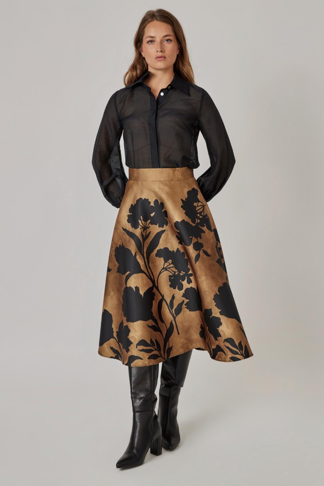 Model trägt Rock mit Blüten-Scherenschnitt-Print und Seitentaschen, kombiniert mit transparenter Bluse, Frontansicht. 