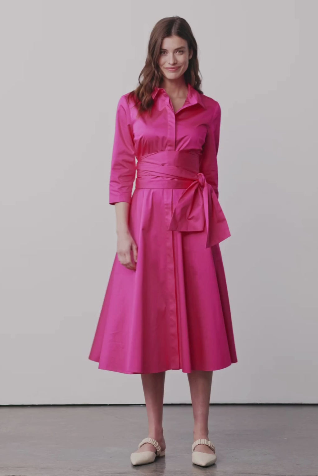 Modell dreht sich und trägt ein Blusenkleid mit Bindegürtel in einem leuchtenden Pink 