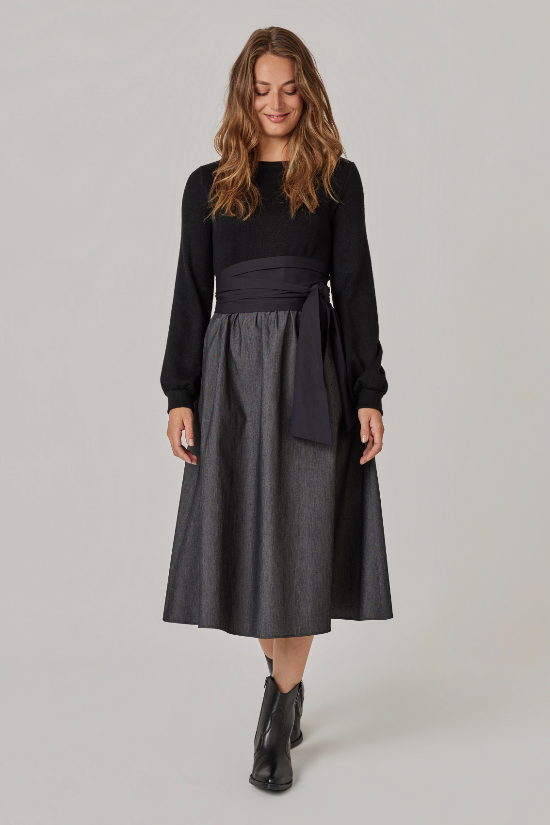 Model trägt Strick-Mix-Kleid mit Bindegürtel und ausgestelltem Rock, Frontansicht.
