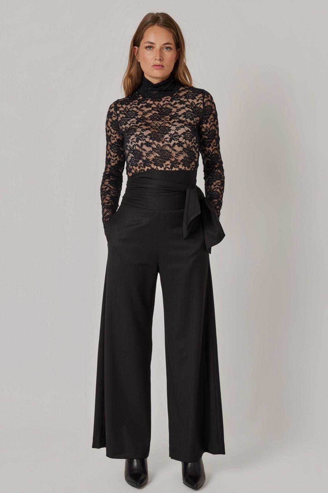 Model trägt schwarze Weite Hose mit Bindegürtel, kombiniert mit Spitzenoberteil, Frontansicht.