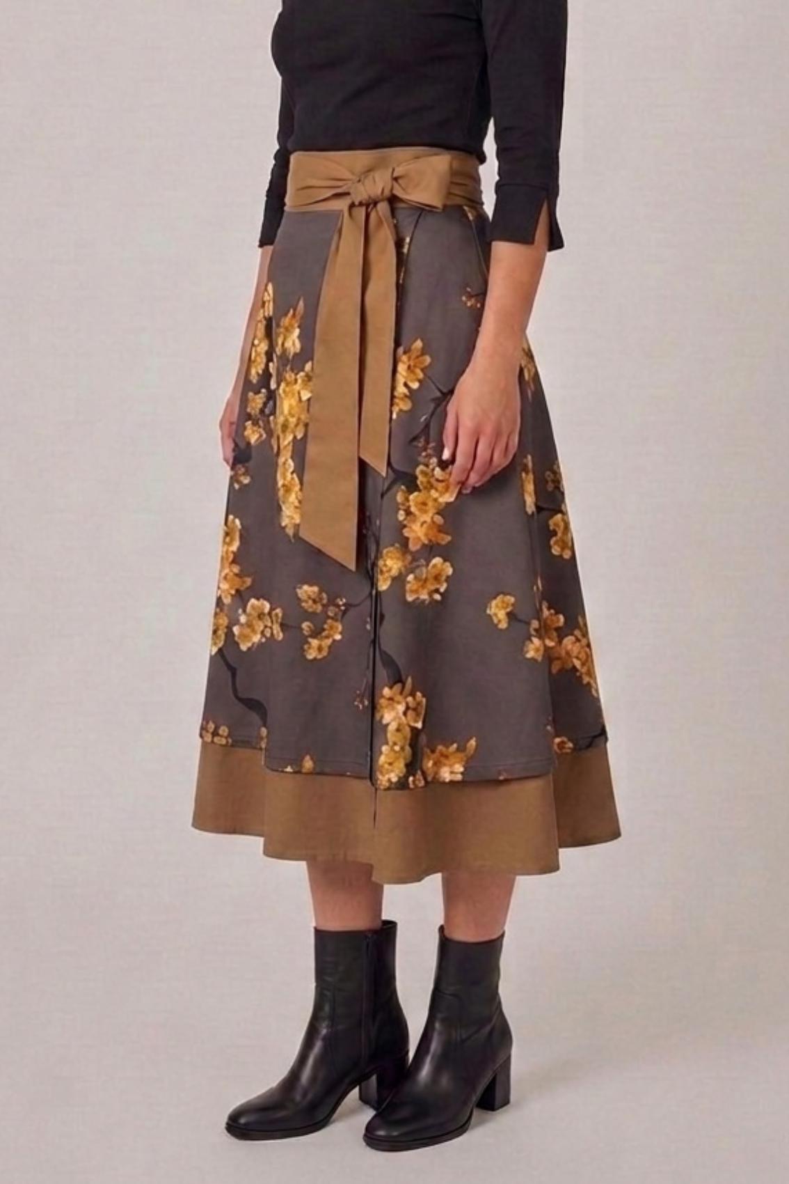 Model trägt Wickelrock mit Kirschblütenprint und seitlich gebundener Schleife in Karamell, Seitenansicht von schräg vorn.